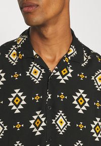Kortärmad skjorta i svart tyg med ett geometriskt mönster i vitt och gult, med knapplist fram och design av campkrage.