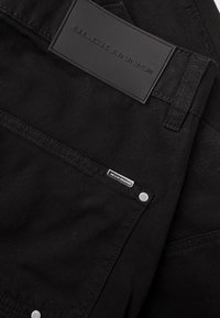 Zwart denimstof met een gladde textuur. Beschikt over een groot, geperst rechthoekig label en een klein metalen label op de voork pocket.
