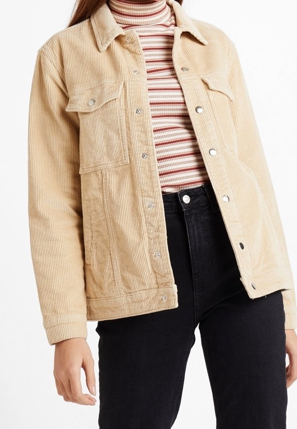 Veste en velours côtelé beige avec boutons-pression portée sur un col roulé rayé rouge, blanc et beige, associée à un jean noir taille haute.