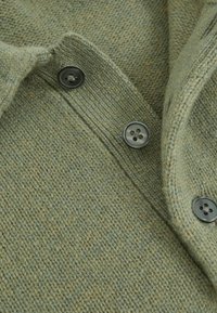 Zelený vlněný cardigan se strukturovaným pletením, s šálovým límcem a třemi černými knoflíky na přední straně pro zapínání.