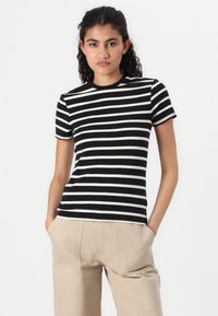 T-shirt a maniche corte a righe nere e crema con scollatura rotonda, realizzata in tessuto morbido, abbinata a pantaloni beige neutri.