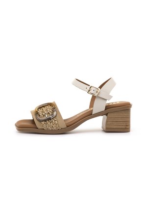 Sandale beige à bout ouvert avec une bride avant tissée présentant une grande boucle décorative, bride blanche à la cheville avec boucle dorée, et talon bloc.