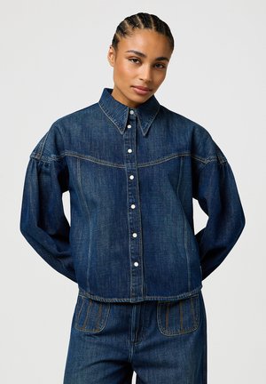 Denim jacket in dark blue with a button-up front, pointed collar, and voluminous sleeves. Features contrasting stitching and a cropped design.