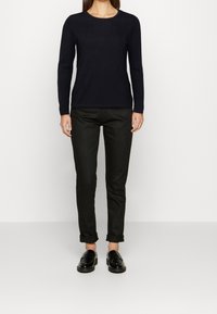 Zwarte langarmshirt, slim fit, gecombineerd met donkergroene broeken en zwarte instappers. Eenvoudig ontwerp, geen zichtbare patronen of accenten.