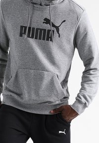 Šedá mikina s kapucí, s velkým černým logem "PUMA" a grafikou skákající pumy. Obsahuje přední kapsu typu klokan a žebrované manžety.