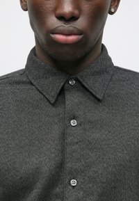 Chemise boutonnée texturée gris foncé avec un col pointu, dotée de deux boutons au cou et d'un motif subtil en chevrons.