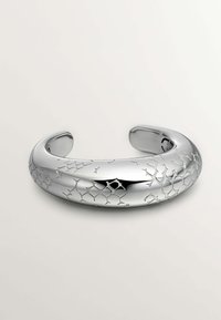 Pulsera de brazalete de plata con una superficie lisa y pulida, y patrones geométricos texturizados grabados en un lado. Extremidades redondeadas y abiertas.