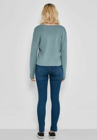 Maglione azzurro chiaro a maniche lunghe con vestibilità comoda, abbinato a jeans scuri aderenti e sneaker nere. Design semplice, senza motivi visibili.