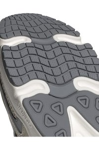 Šedá gumová podrážka obuvi s texturovaným povrchem, která obsahuje trojúhelníkové a obdélníkové vzory pro lepší přilnavost, doplněná bílými akcenty.