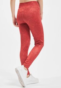 Leggings rossi con un motivo a foglia testurizzato, vita alta e finitura liscia, abbinati a sneakers bianche con una suola testurizzata.