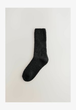 Crna, pahuljasta čarapa s mekim teksturom, koja ima rebrasti rub i zaobljeni vrh. Dizajn je jednostavan i ujednačen kroz cijelu čarapu.