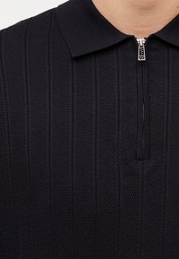 Μαύρο πλεκτό πόλο μπλουζάκι με κάθετες υφασμάτινες ρίγες και ασημί φερμουάρ στο γιακά που δείχνει το λογότυπο AX.