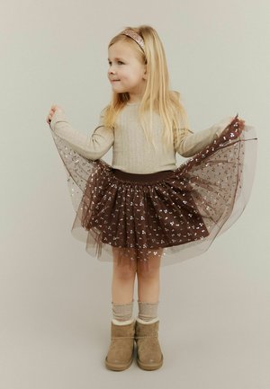 Hnědá tylová sukně se stříbrnými akcenty vrstvená přes pevný hnědý základ, v kombinaci s béžovým dlouhým rukávem a hnědými botami.