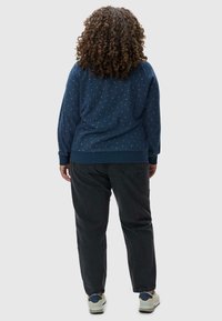Felpa blu navy con un motivo testurizzato e polsini a costine, abbinata a pantaloni scuri e sneakers chiare. Vista da dietro.
