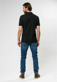 Black polo shirt with short sleeves, paired with blue denim jeans. The shirt features a classic collar and a simple design.