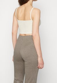 Bílý krátký top na tenkých ramínkách spojený s vysokým pasem kostkovaných kalhot v hnědé a krémové barvě. Texturovaná látka, přiléhavý střih.