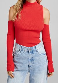 Röd ribbad topp med hög hals och kalla axlar, långärmad, som matchar med ljusblå högmidjade jeans.