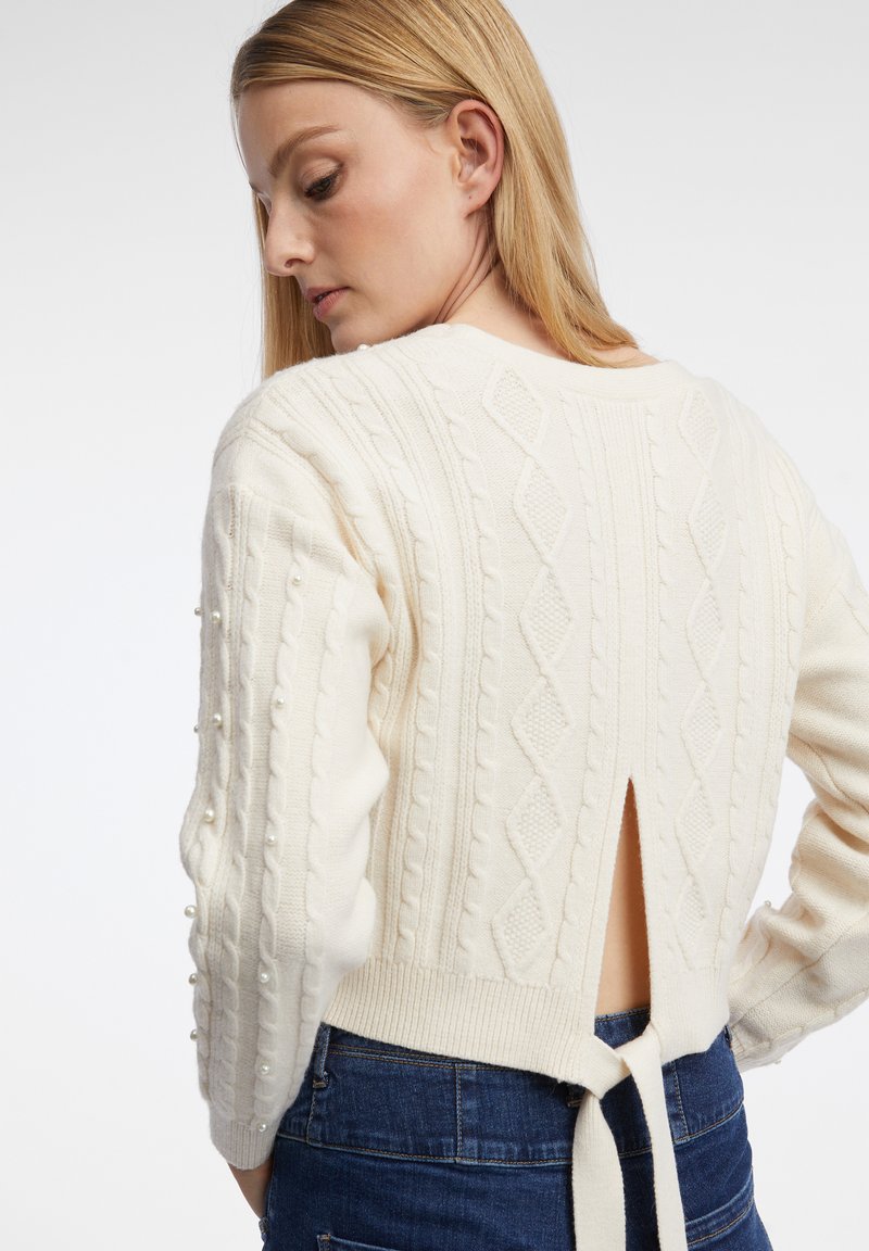 Pull en maille torsadée crème avec une ouverture dans le dos, un détail à nouer et des accents en perles sur les manches, avec des poignets et un ourlet côtelés.