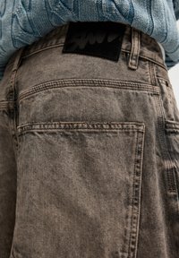 Harmaat denimit, joissa on tekstuuripinta, mustalla nahkapaikalla logoyksityiskohdalla takana ja tavalliset taskut.