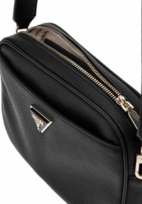 Sac en cuir noir à porter en bandoulière avec un fini texturé, doté d'une fermeture éclair dorée et d'un accent en métal en forme de triangle à l'avant.