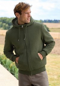 Hoodie aus grünem, weichem Material mit Reißverschluss, zwei Taschen und gerippten Bündchen und Saum.