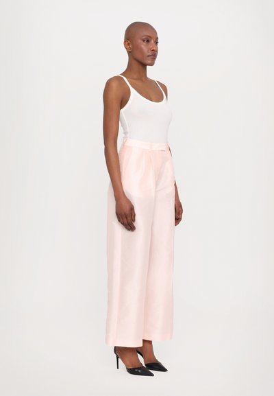 Light pink satin wide-leg pants with a belted waist, paired with a white tank top and black pointed heels. Smooth texture and tailored fit.