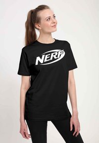 Czarna koszulka z krótkim rękawem, z dużym białym logo "NERF" na przodzie. Okrągły dekolt i luźny krój. Gładka faktura materiału.