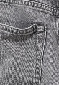 Gros plan d'un tissu en denim gris délavé montrant la couture cousue et le bord d'une poche arrière avec texture et tissage visibles.