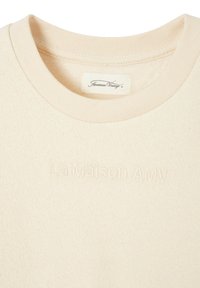 Beige sweatshirt i ett texturerat fleece-material, har en ribbad rund halsringning och ett präglat logo "La Maison AMY" på framsidan.