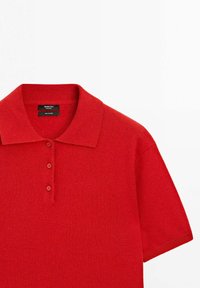 Polo shirt rosso a maniche corte con tre bottoni e colletto a coste, realizzato in 100% cashmere, steso su uno sfondo bianco.