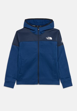 Sudadera con capucha azul con cremallera completa, canesú azul marino oscuro, bolsillos frontales, capucha y logotipos blancos de The North Face en el pecho y la manga izquierda.