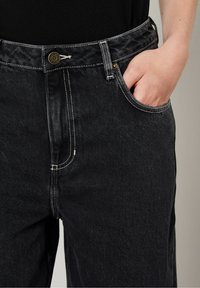 Zwarte denim jeans met een hoge taille, zichtbare stiksels, een voorzak en een metalen knoopsluiting. Zachte textuur met een rechte pijpdesign.