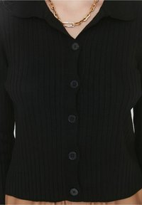 Černý žebrovaný pletený cardigan s knoflíkovým zapínáním vpředu, límcem a texturovanou látkou. Ozdoben kulatými černými knoflíky.