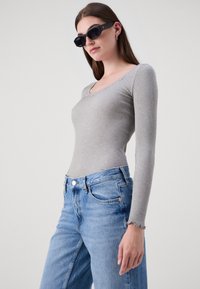 Grå ribbet langermet topp med rund hals, kombinert med lyseblå høyhåndte jeans med frynsete kanter. Svart solbriller som tilbehør.