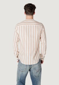 Camicetta leggera a maniche lunghe con strisce verticali beige e bianche, dettagli con bottoni e orlo dritto, abbinata a jeans blu.