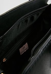 Interno di una borsa sintetica nera con tasche con cerniera, tessuto liscio e un'etichetta logo visibile con la scritta "ANNA FIELD".