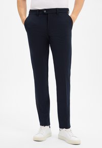 Granatowe spodnie od garnituru o gładkiej teksturze, z zapięciem na guzik, bocznymi kieszeniami i slim fit, zestawione z białymi trampkami.