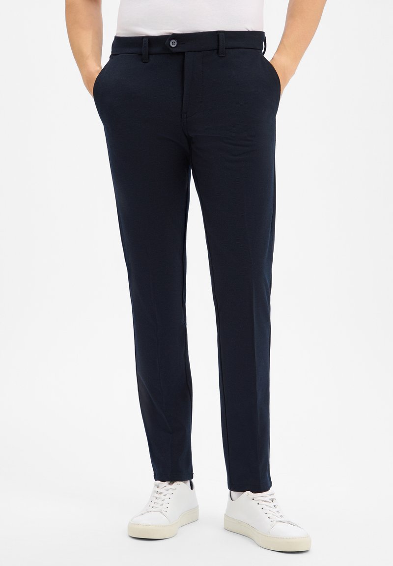 Granatowe spodnie od garnituru o gładkiej teksturze, z zapięciem na guzik, bocznymi kieszeniami i slim fit, zestawione z białymi trampkami.