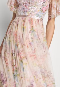 Gros plan d’une personne portant une robe plissée à fleurs pastel en tissu transparent avec des manches courtes bouffantes couvertes de sequins.