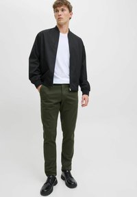 Czarna kurtka bombowiec z zamkiem, biała koszulka, oliwkowe spodnie slim-fit i czarne buty na sznurowadła, stojący na jednolitym tle.
