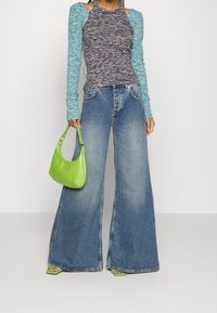 Långärmad, flerfärgad stickad topp med sidoklipp, i kombination med vida blå jeans och en ljusgrön handväska, med släta texturer.