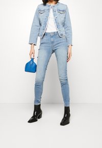 Chaqueta de mezclilla azul claro con bordes deshilachados, combinada con jeans ajustados a juego, botas negras con tacón bloque y un pequeño bolso azul.