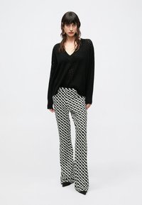 Musta kootud pikki varrukaid kampsun V-kaelusega ja avatud koemustriga, kombineeritud kõrge vöökohaga laienevate pükstega, millel on valge geomeetriline trükk.