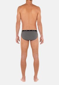 Grå herrunderkläder med svart elastisk midjeband, slät textur och kroppsnära design, sedd bakifrån.