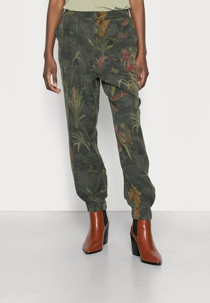 Grün camouflagegemusterte Hose mit floralen Akzenten, elastischen Bündchen und Seitentaschen. Kombiniert mit braunen Stiefeletten mit Absätzen.