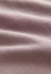 Tela de malva pálido con una textura suave, que presenta un sutil estiramiento y una construcción de punto fino, mostrando pliegues y arrugas suaves.