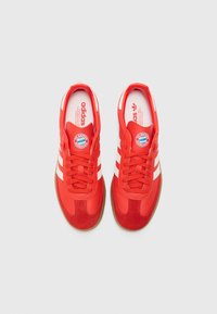 Röda sportskor med vita ränder, överdel i mocka och syntetmaterial, strukturerad gummisula, med FC Bayern München-logotyp på tungan.