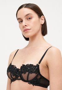 Schwarzer Spitzen-BH mit transparenten Mesh-Cups, floralen Stickereien, Satinakzenten, verstellbaren Trägern und Unterstützung durch Bügel.