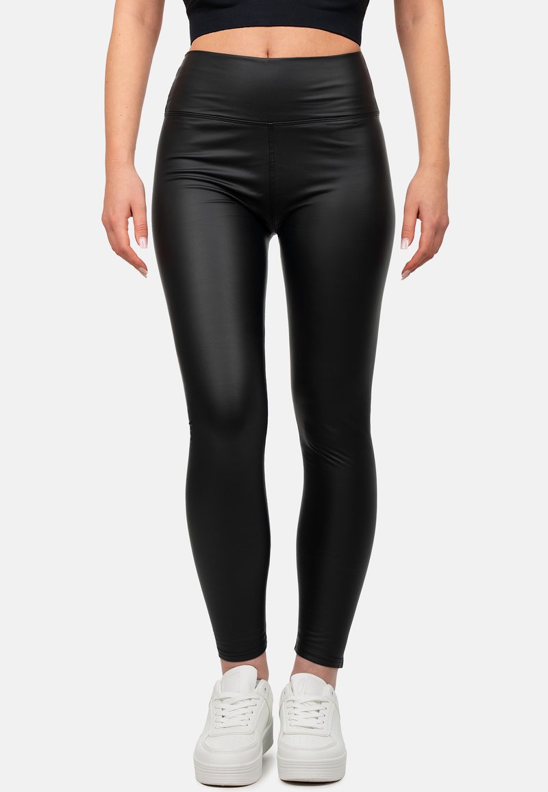 Leggings neri in ecopelle con una vita alta, caratterizzati da una texture liscia e una vestibilità aderente, abbinati a sneaker bianche.