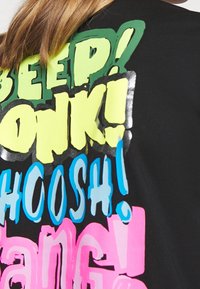 Sort t-shirt med iøjnefaldende, farverig grafisk tekst i grøn, gul, blå og pink, med tegneserie-lignende udtryk som "BEEP!" og "POW!"